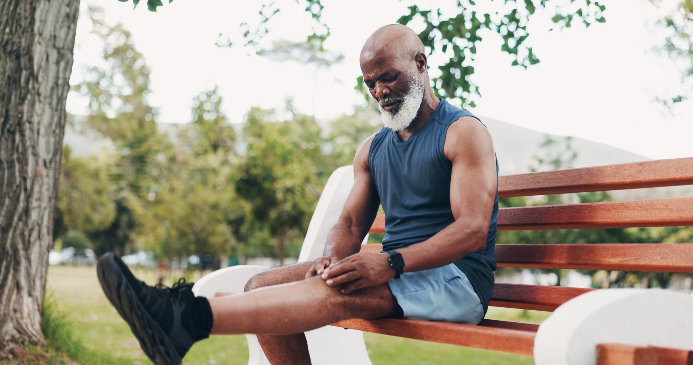 Older man on a park bench holding his knee in pain after activity