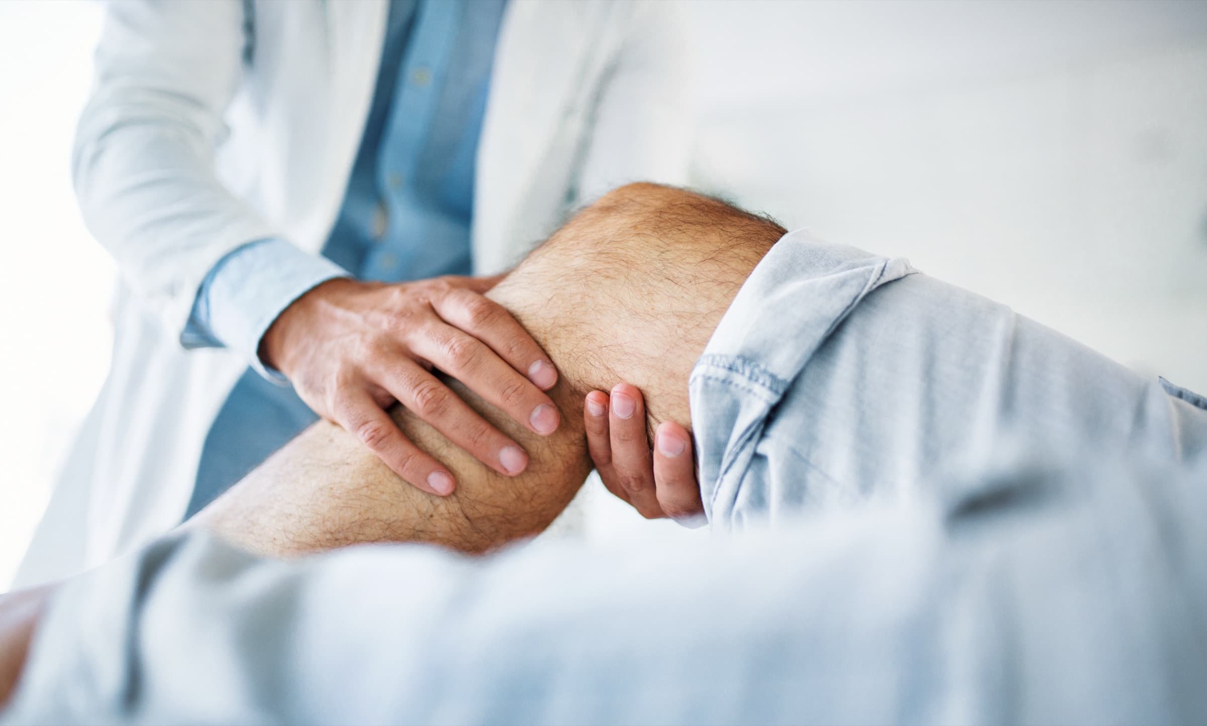 Physician's hands examining a patient's knee during a clinical assessment